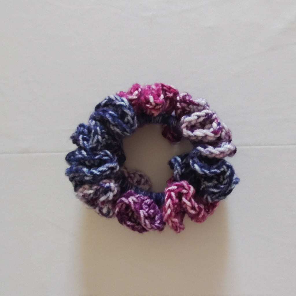 Multicolor crochet scrunchie in violet, pink, blue, and white soft acrylic yarn, displayed flat on a white background