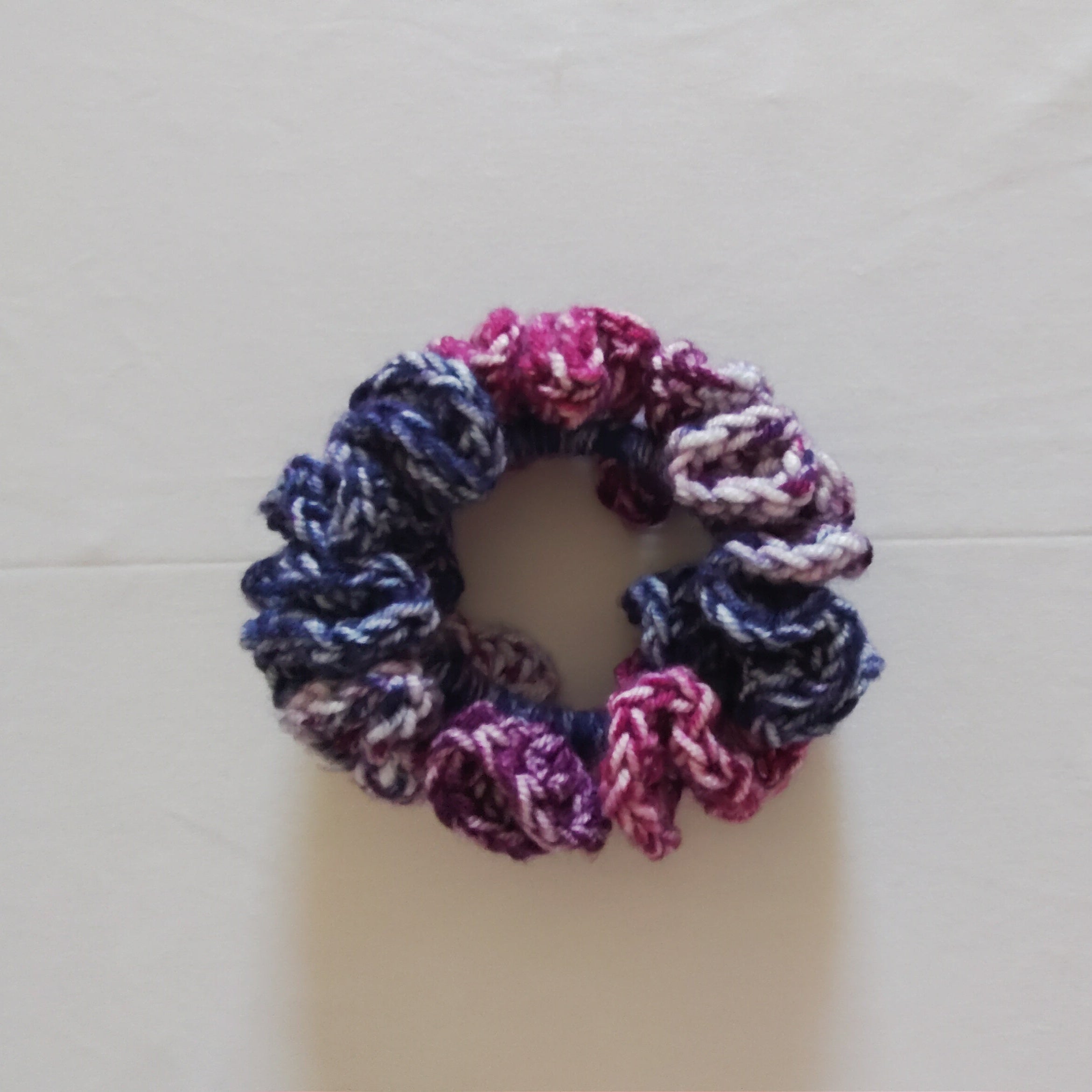 Multicolor crochet scrunchie in violet, pink, blue, and white soft acrylic yarn, displayed flat on a white background