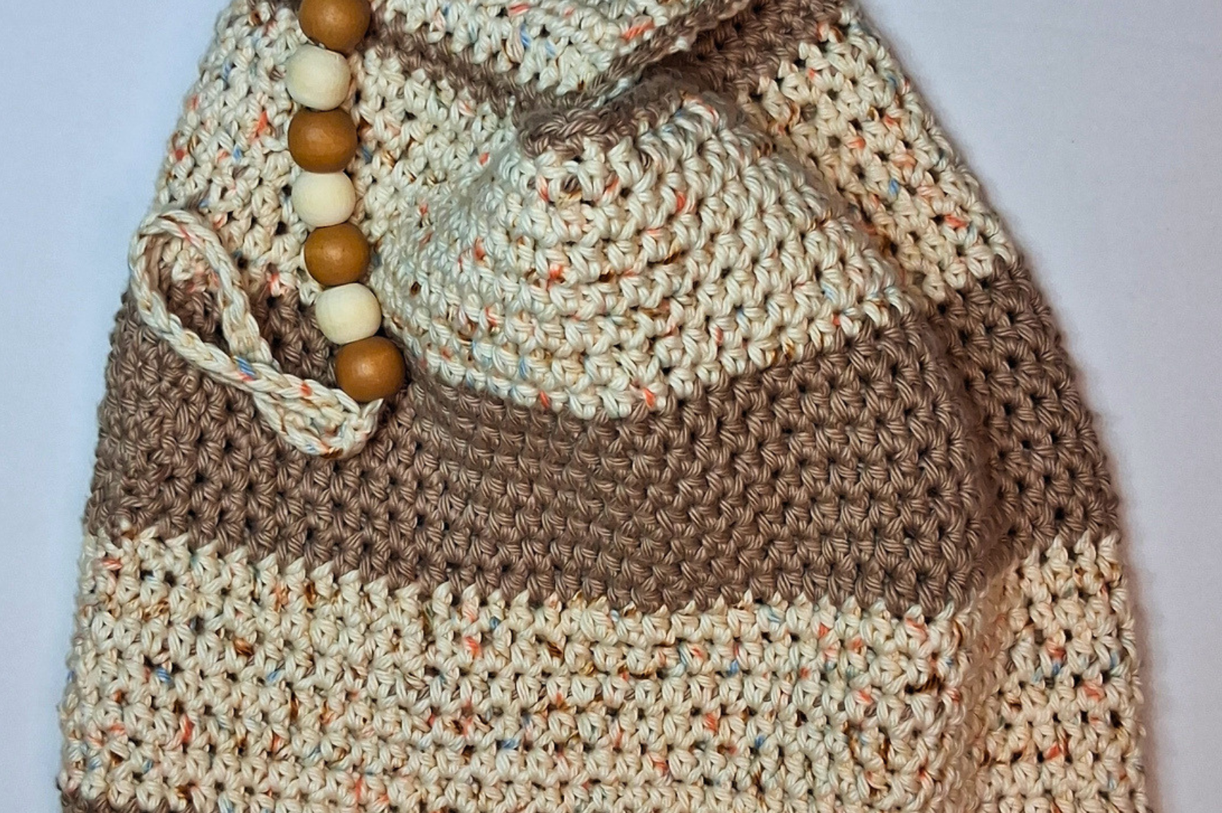 Close-up of a medium crochet Japanese knot bag in beige and spunky sand striped 100% cotton with natural wood round beads and keychain loop embellishment